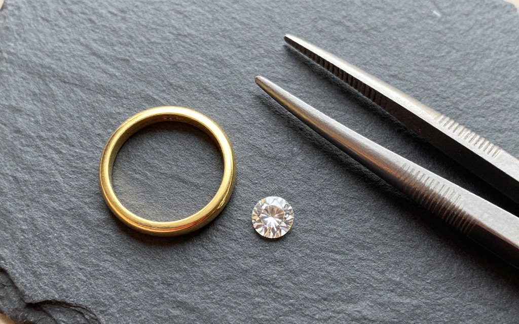 A gold ring beside a loose diamond, showing carat vs karat as weight versus gold purity.